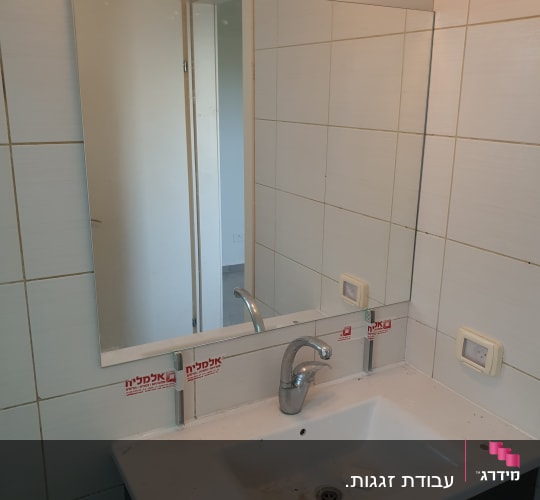 מראה מלבנית מעל כיור בחדר אמבטיה